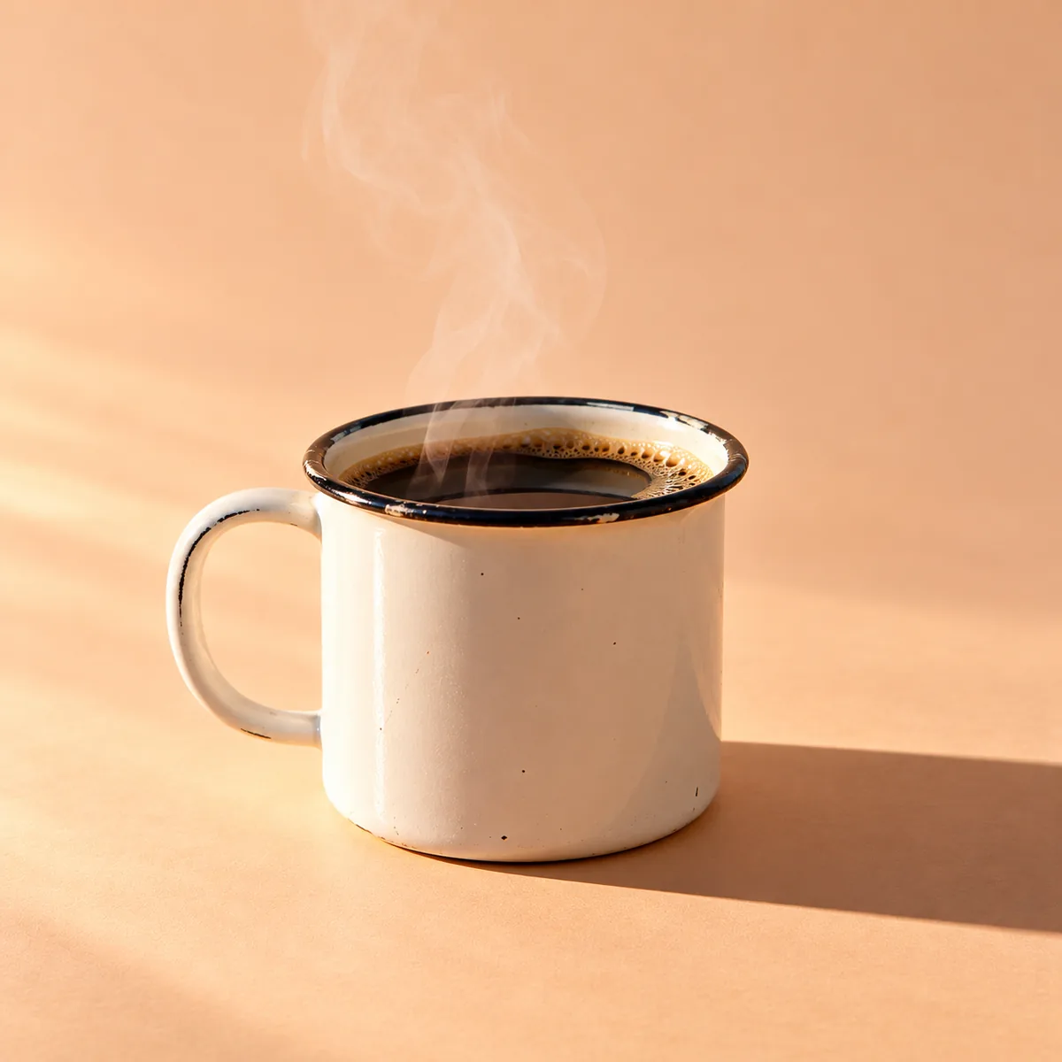 A white enamel mug of steaming black coffee in early morning light.